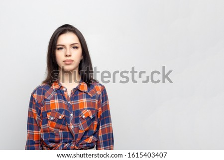 Portrait young beautiful woman not smiling in plaid shirt isolated on white-gray background. Girl with minimal natural make-up on her face. The photo is not retouched with natural defects on the skin.