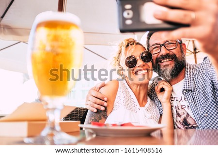 Cheerful happy people couple at the restaurant enjoying and having fun together taking selfie picture with modern phone - hug and relationship love concept for middle age woman and man