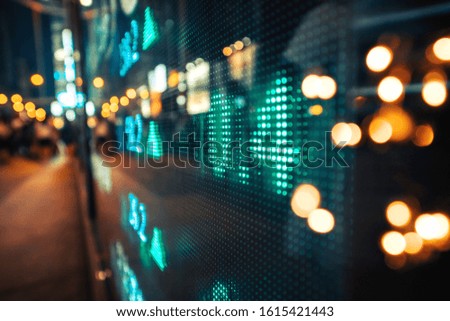 Display stock market numbers and graph with city light reflections at the street. Small focus line, some noise. Blurry.