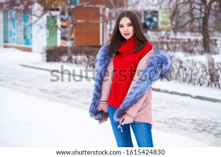 Happy young blonde woman in blue down jacket in winter street