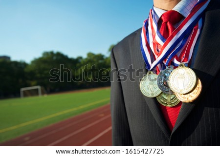 Gold medals draped around the neck of an unrecognizable businessman standing in front of an outdoor running track
