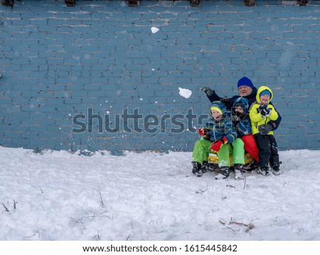 elderly man in bright winter clothes rides three boys in beautiful jackets on yellow sleds. Children love father. Winter games with snow. Kids enjoy spending time on vacation in village