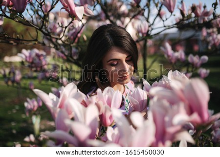 Charming girl stand by the beautiful pink magnolia tree outside. Gorgeous lady
