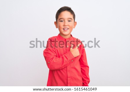 Beautiful kid boy wearing elegant red shirt standing over isolated white background cheerful with a smile of face pointing with hand and finger up to the side with happy and natural expression on face