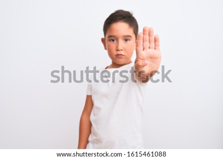 Beautiful kid boy wearing casual t-shirt standing over isolated white background doing stop sing with palm of the hand. Warning expression with negative and serious gesture on the face.