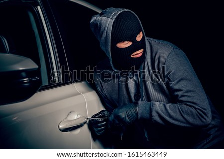 A man with a Balaclava on his head tried to break into the car. He uses a screwdriver. Hijacker, the concept of car theft Royalty-Free Stock Photo #1615463449