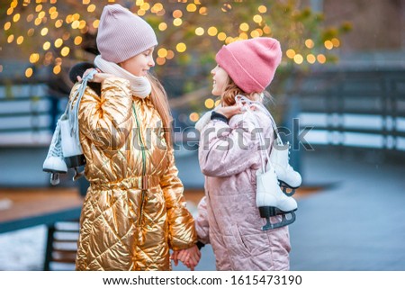 Adorable little girls skating on ice rink outdoors in winter snow day