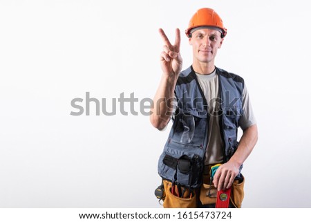 Builder shows a goat sign. In work clothes and hard hat. On a light gray background.