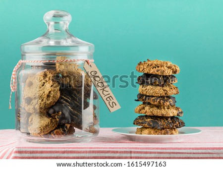 front view of a stack of chocolate and raisin oatmeal cookies and a cookie jar Royalty-Free Stock Photo #1615497163