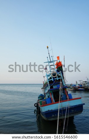 A fishing boat held by ropes facing towards vastness of sky and sea. Shot from behind.