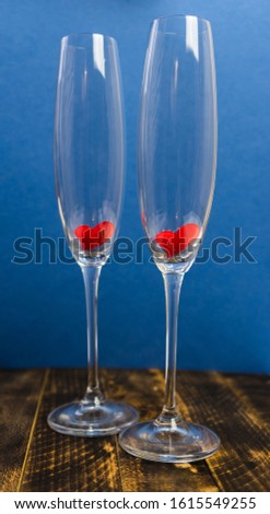 Valentine's day greeting card with champagne glasses and red hearts on wooden table. Blue background