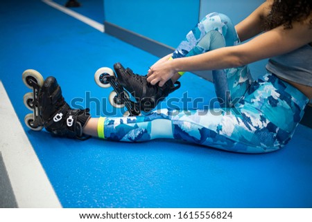 Unrecognizable young skating woman with blue pants on blue wall, tying her shoelaces