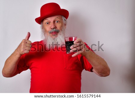 Cheerful elderly gentleman holding a rum cocktail.
Old man wearing a red bowler hat and red shirt holding a drink.