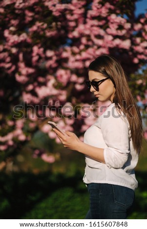 Young woman in white shirt use smartphone outside. Background of pink tree
