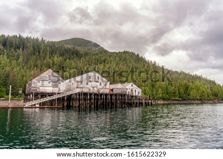 Old fish cannery in Ketchikan, Alaska. Abandoned factory of canned salmon. Tongass National Rain forest is on a background. Seasonal salmon fishing spot. Royalty-Free Stock Photo #1615622329