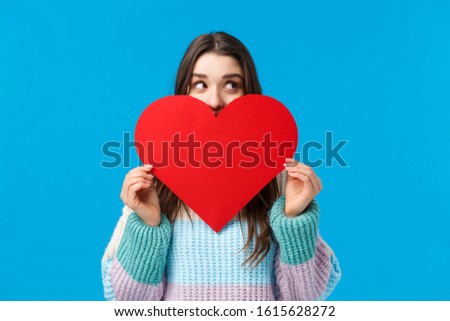 Searching for soulmate, where are you. Cute and romantic girlfriend in sweater, hiding face behind big red heart, looking around, gazing right curious and dreamy, show her love on valentines day
