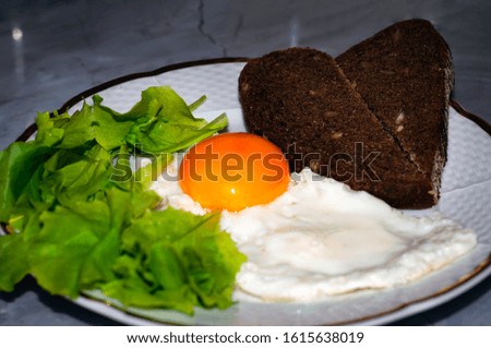 soft focus of white plate with tasty fried egg, dark slices of bread and green spinach on grey marble background