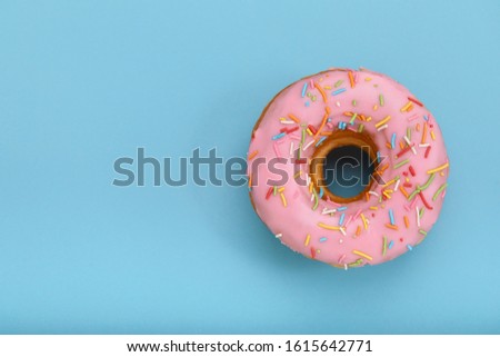Pink donut on a blue background, top view, concept of desserts, pink color on blue. Copy space, blue background.