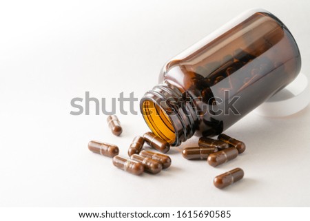 Brown medicine bottle and multiple pills on pure white background