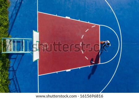An overhead view of a young man throwing the orange ball into the basketball hoop on an outdoor court