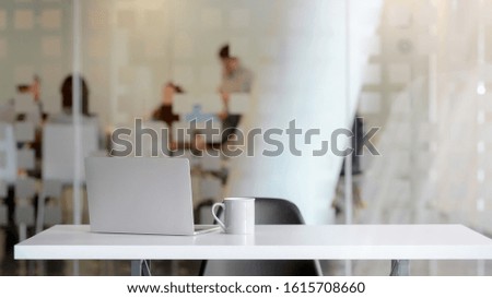 Close up view of simple workspace with blank screen laptop, coffee cup and copy space on white table with blurred office room background 