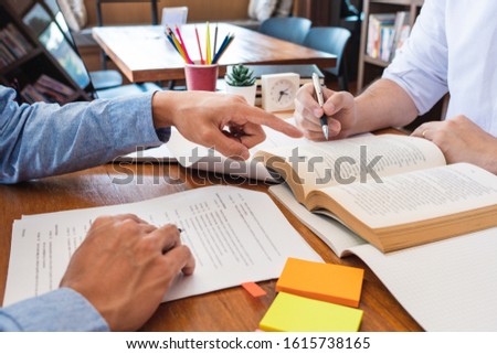 tutor and college students teaching school work and explaining problem solution studying and reading together in a table at class room