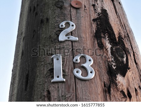 Power pole with numbers 2, 1 and 3 attached.  Rough surface with tar visible.