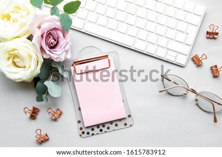 Home office desk workspace with blank paper clipboard and  pink roses bouquet  on white background. Flatlay, top view.