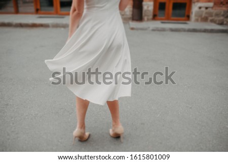 a woman without a face in a white simple dress of midi length is spinning and the dress is spinning in different directions on the street against the asphalt