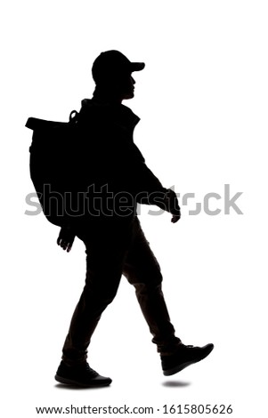 Silhouette of a man wearing a backpack looking like a traveler or hiker trekking. He is walking or hiking 
