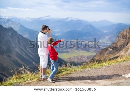 Young father and his teenager son taking pictures of a beautiful valley in the mountains