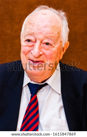 Portrait of happy white elderly man with dark suit, white shirt and striped blue red tie smiling on bright brown background Royalty-Free Stock Photo #1615847869