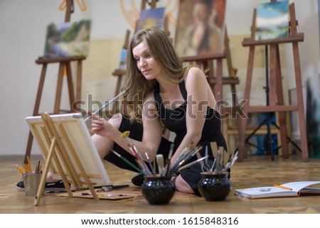 Artist in the art studio drawing on the estel stand sitting on the floor.