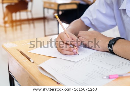 Asian Students holding pencil in hand doing multiple-choice quizzes or testing exams answer sheets exercises on old wood table In secondary school, college university classroom in education concept. Royalty-Free Stock Photo #1615871260