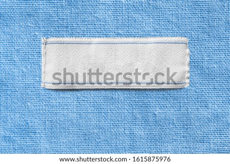 White blank textile clothes label on blue linen background closeup