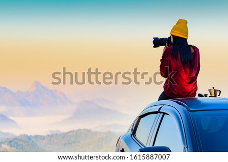 Woman traveller photographer sitting to takes a photo shot on her owns roof of the car with scenery view of the mountain and mist morning in background