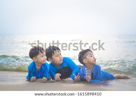 A boy is playing sand and swimming with his brothers on the beach.