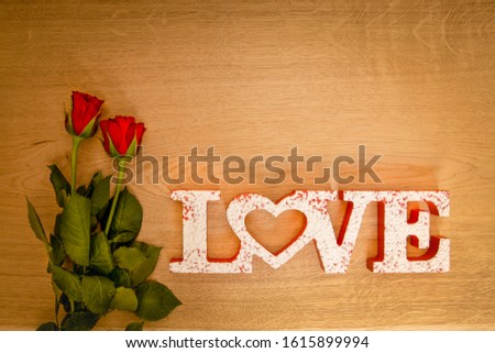 Two red roses with love lettering on a wooden background.