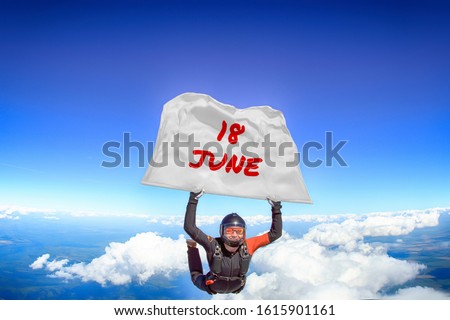 18 June. Parachutist flies a flag with date of June 18. Skydiver in black suit. Extreme as a way of life. 
 Royalty-Free Stock Photo #1615901161