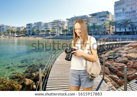 Beautiful smiling woman holding modern equipment for photography hobby on beach. Spain vacation concept.