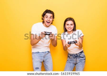 Photo of caucasian couple man and woman playing together video games using joysticks isolated over yellow background