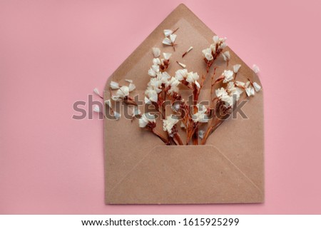 Flowers in an open envelope from kraft paper on a pale pink background. The message of Valentine's Day, Women's Day, wedding. Flat lay, top view