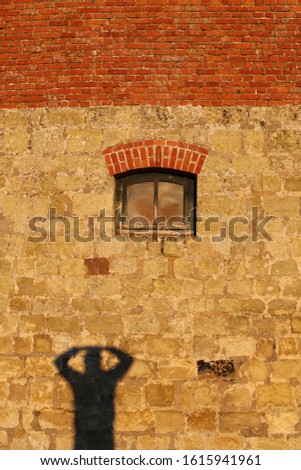Close up outdoor view of the silhouette shadow of a man drawn on a stone wall house. Dark human shape visible on a facade building during a sunset. Abstract picture of a rough lighted surface.