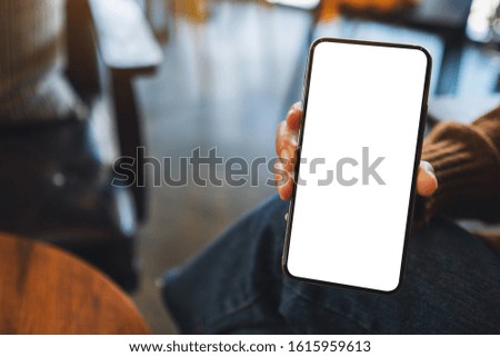 Mockup image of a woman holding and showing black mobile phone with blank screen in cafe