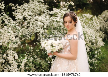 Charming bride in gorgeous wedding dress hold bouquet and stand in front of blooming trees