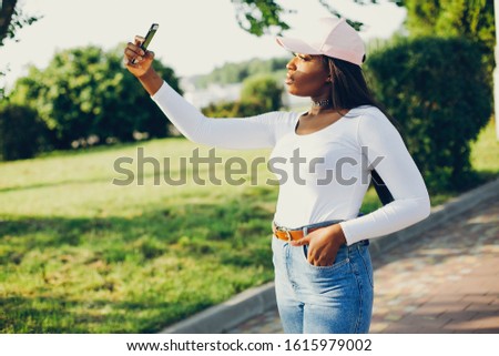 Stylish girl in a summer park. Woman in a blue jeans and pink cap. Famale with smartphone