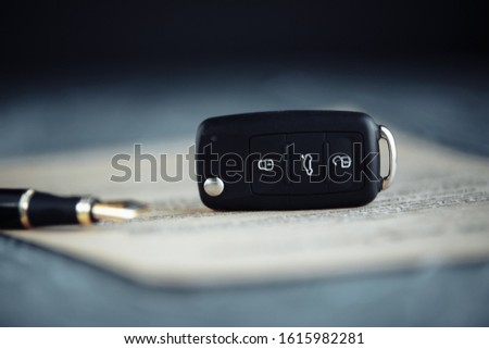 Black car key and money on a signed contract of car sale.