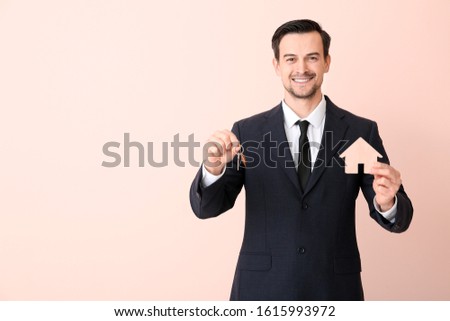 Male real estate agent with key on color background