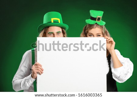 Young couple with blank poster on color background. St. Patrick's Day celebration