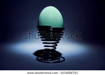 A green/blue egg in an egg cup underneath a spot light
